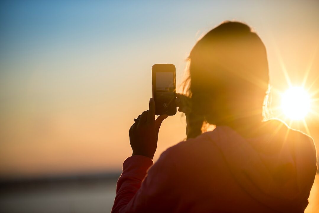 woman taking photo of sunset using smartphone camera