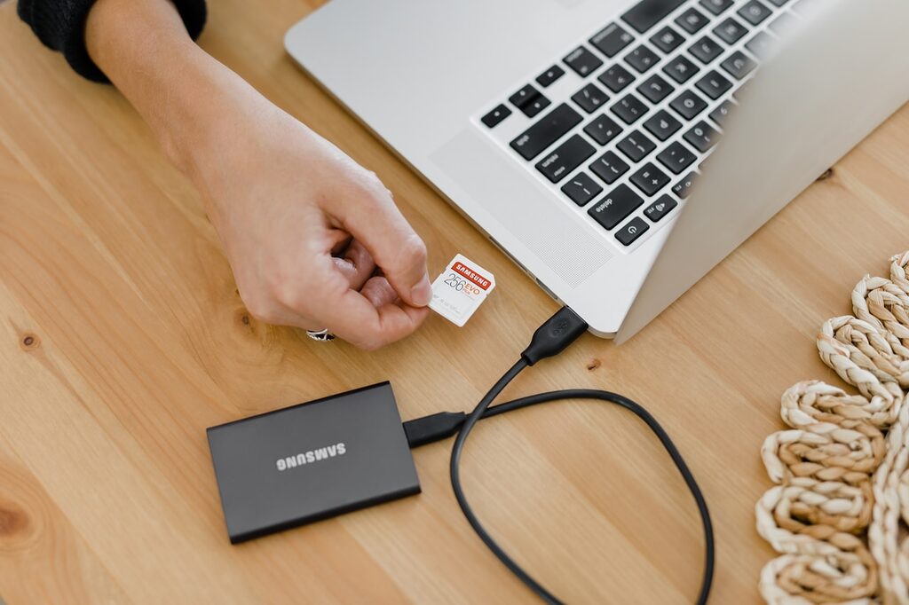 person holding black and silver laptop computer with external SSD solid state drive USB