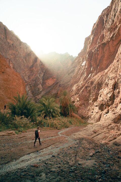 a man walking down a dirt road next to a mountain travel